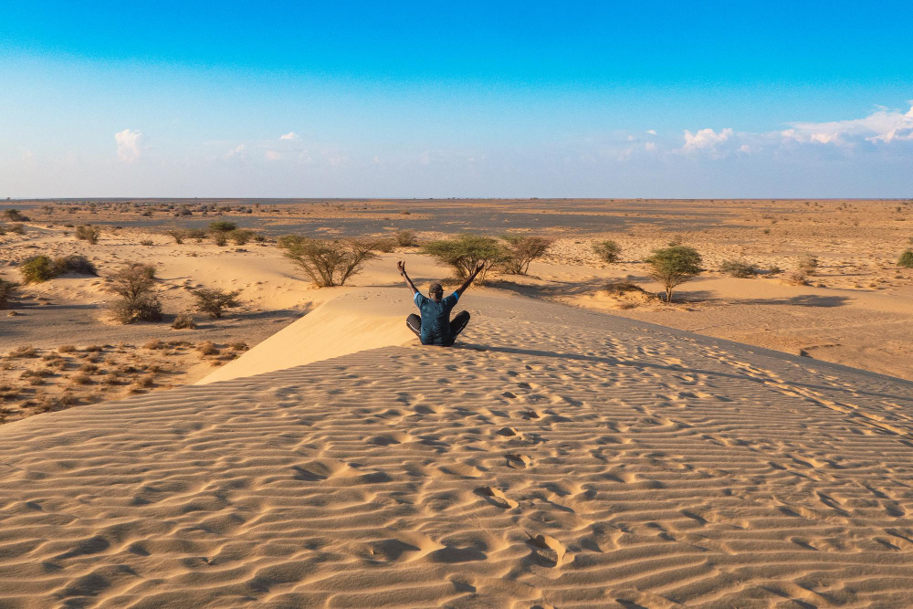 rear-view-man-sitting-with-arms-outstretched-sand-dune-north-horr-sand-dunes-kenya
